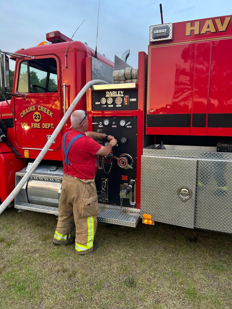 A Crains Creek firefighter at the pump panel of the tanker, charging a hose line.